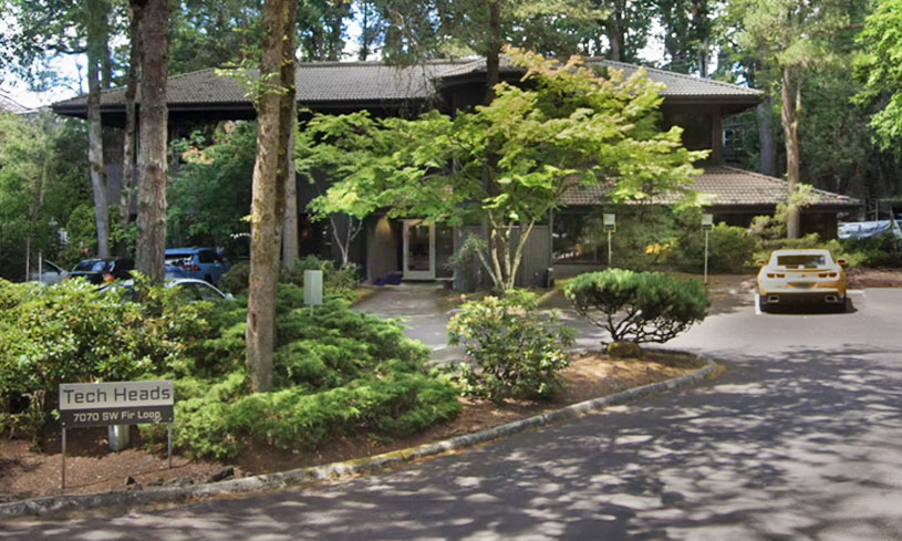 Tech Heads office building surrounded by trees and landscaping with parking area in front.